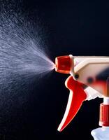 Close-up of a Spray Bottle Actively Dispensing Water Mist in a Dark Background Highlighting the Nozzle Design and Spraying Action photo