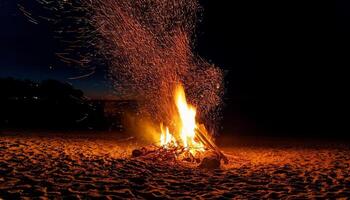 Nighttime Beach Bonfire Creates Glowing Sparks Under a Dark Sky While People Enjoy the Warmth and Ambiance of the Fire photo