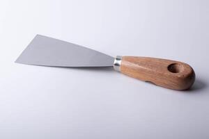 metal spatula with wooden handle lies on white surface, showcasing its simple and functional design. spatula blade is flat and wide, ideal for spreading or scraping tasks in cooking or baking photo