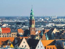 Aerial view of Wroclaw, Poland, featuring the Gothic style Old Town Hall tower with a green spire, surrounded by historic red tiled buildings and modern structures. photo