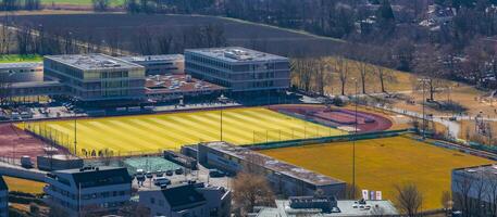Aerial view of a sports complex in Salzburg, Austria, featuring a yellow and green football field, red running track, modern buildings, and surrounding greenery. photo