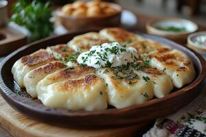 a traditional Eastern European table setting with freshly baked pierogi served on a rustic wooden plate, garnished with sour cream and herbs photo
