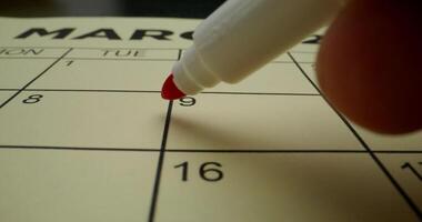 A person is writing on a calendar with a red marker photo