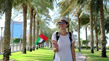 Woman tourist holding small UAE flag against Corniche Walking Trail in Abu Dhabi. Blend of nature, patriotism, and serenity, with lush greenery , views symbolizing harmony and progress. video