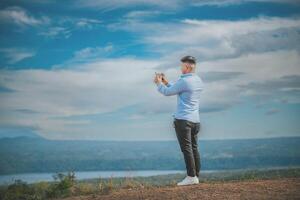 Young man taking photos with cell phone at a natural viewpoint. Tourist taking photos with phone at a volcanic viewpoint, Masaya, Nicaragua