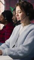 Vertical Call center team of agents wearing headset assisting customers over phone at modern workstation with multiple monitors, emphasizing customer support, communication and service efficiency, camera A video
