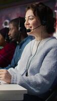 Vertical Friendly call center employee talking in audio headset, assisting customers in office. Happy customer support operator communicating with clients during telephone call, camera B close up video