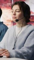 Vertical Teamworking call center coworkers in office helping customers by answering questions. Team of agents in customer support workplace in front of PC using headset mic to talk with clients, camera A video