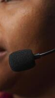 Vertical Closeup of call center employee talks in headphones mic, handling customer inquiries and complaints in office. African american customer service representative assists customers with issues, camera A video