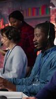 Vertical Call center operator next to coworkers dealing with upset customers, speaking using headset at office desk. Teamworking staff members doing customer support job, handling clients complaints, camera B video