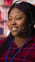 Vertical Upbeat call center agent provides guidance to customers, answering questions. Jolly African american customer center worker at PC desk walking clients through technical solutions during call, camera A video