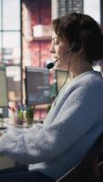vertical ligar Centro equipe do agentes vestindo fone de ouvido ajudando clientes sobre telefone às moderno posto de trabalho com múltiplo monitores, enfatizando cliente apoiar, comunicação e serviço eficiência, Câmera b video