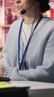Vertical Call center worker speaking in audio headset microphone, using remote access tools. Woman in customer center assisting clients with installing software, communicating through headphones mic, camera A video
