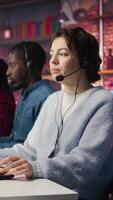 Vertical Teamworking call center coworkers in office helping customers by answering questions. Team of agents in customer support workplace in front of PC using headset mic to talk with clients, camera B video