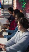 Vertical Customer support workplace coworkers managing incoming and outgoing calls. Teamworking call center agents in front of PC in office using headset mic to answer customers questions, camera B video
