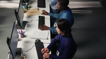 Call center coworkers in diverse office helping customers, aerial shot. Teamworking employees in customer center workspace assisting clients needing help resetting password video