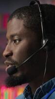 Vertical Smiling call center agent dealing with unhappy customers, speaking with them using audio headset at office desk. Customer support worker handling clients complaints in company workspace, camera A video