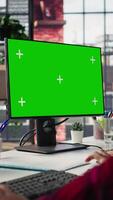 Vertical Call center employee working on green screen mockup PC, doing account management in office. Customer support agent in front of chroma key isolated screen computer handling calls, camera B close up video