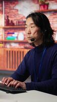 Vertical Call center agent speaking in audio headset microphone, using remote access tools. Worker in customer center assisting clients with installing software, communicating through headphones mic, camera B video