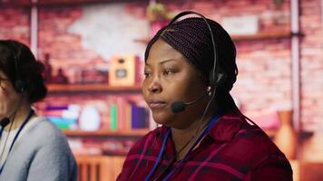 Happy call center agent providing step by step guidance to customers. Smiling customer center worker at PC desk walking clients through technical solutions during call, camera A video