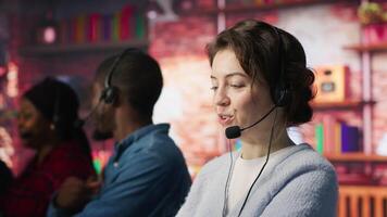 Cheerful call center employee wearing audio headset assisting customers in office. Upbeat woman at work doing customer support, communicating with clients in telephone call, camera A close up video