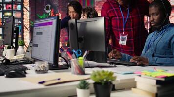 Smiling multiethnic technical support team in diverse call center office doing troubleshooting. Cheerful multiracial IT staff members fixing customer connectivity issues, camera B video