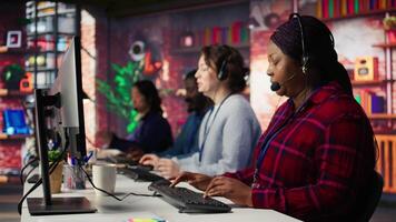 Happy call center agent providing step by step guidance to customers. Smiling customer center worker at PC desk walking clients through technical solutions during call, camera B video
