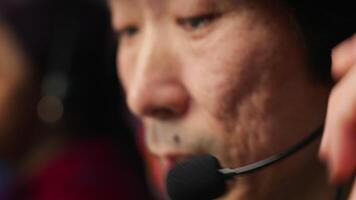 Closeup of experienced worker talking with customer using headphones mic to gain new sales. Asian account manager in office using audio headset, speaking with client to generate leads, camera A video