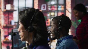 Call center operator next to coworkers dealing with upset customers, speaking using headset at office desk. Teamworking staff members doing customer support job, handling clients complaints, camera A video
