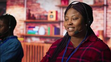 Upbeat call center agent provides guidance to customers, answering questions. Jolly African american customer center worker at PC desk walking clients through technical solutions during call, camera A video