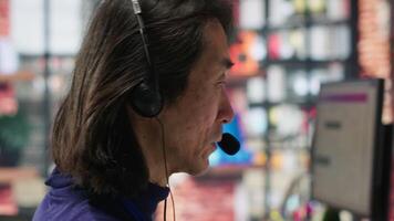 Closeup of senior call center agent helping customers regain access to accounts, resetting passwords. Experienced Asian worker in diverse customer center assisting clients needing help, camera A video