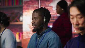 Portrait of smiling technical support specialist in call center office doing troubleshooting. Upbeat african american IT worker fixing customer connectivity issue, using headphones, camera A video