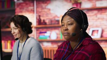 Customer center employee gesturing loud colleague to quiet down during conversation with client. Call center worker upset by noises in office while talking to customers using headphones mic, camera A video