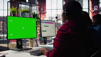 Call center worker solving customers issues using green screen PC. Customer support staff member in front of chroma key computer display using headset to talk with clients, camera B video