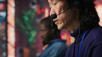 Call center coworkers dealing with upset customers, speaking with them online using headset at office desk. Asian man using PC to do customer support job, handling clients complaints, camera A video