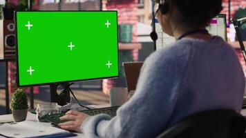 Call center employee working on green screen mockup PC, doing account management in office. Customer support agent in front of chroma key isolated screen computer handling calls, camera A close up video