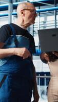 Vertical Smart factory senior engineer teaches intern to implement automated workflows, computerizing manual operations. Experienced man helping trainee integrate sensors into production, camera A video