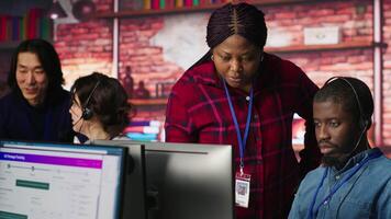 Smiling multiethnic technical support team in diverse call center office doing troubleshooting. Cheerful multiracial IT staff members fixing customer connectivity issues, camera A video