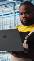 Vertical Industry 4.0 industrial plant engineer automating robotic machines using AI technology. African american man implementing AI features in smart factory using notebook, camera A video