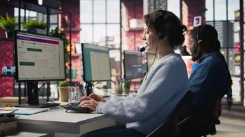 Call center team of agents wearing headset assisting customers over phone at modern workstation with multiple monitors, emphasizing customer support, communication and service efficiency, camera B video