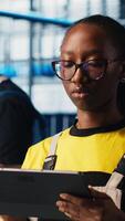 Vertical Industry 4.0 plant technician monitors system performance using digital device app. Smart factory engineer oversees operation of robotic arms and conveyor belts using software on tablet, camera A video