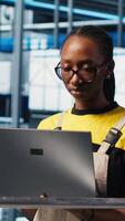 Vertical Smart factory engineer oversees operation of robotic arms and conveyor systems on facility floor. Industry 4.0 plant technician monitors system performance and troubleshoots issues, camera A video