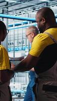 Vertical Industry 4.0 industrial plant engineering team controlling automated machinery using tablet, ensuring workflow continuity. Teamworking smart factory colleagues manage robotic arms, camera A video