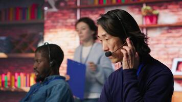 Call center senior agent providing step by step guidance to help customers. Asian experienced customer center worker at PC desk walking clients through technical solutions during call, camera A video