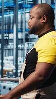 Vertical Smart photovoltaics factory expert looking at system performance metrics on laptop software. African american solar panels plant worker tracking energy production through IoT sensors, camera A video