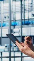 Vertical Senior engineer in smart photovoltaics factory looking at system performance metrics on tablet. Experienced solar panels plant worker tracking energy production through IoT sensors on device, camera A video