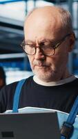 Vertical Smart factory senior engineer uses laptop to oversee operation of robotic arms and conveyor systems. Experienced industry 4.0 plant technician monitors system performance using notebook, camera A video