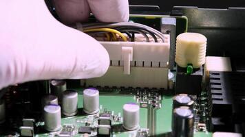 A gloved hand connects wires to a computer motherboard during hardware assembly or repair, focusing on precise technical work. video