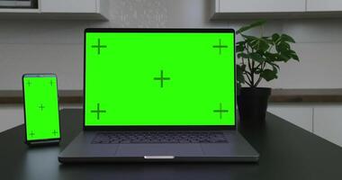 A laptop and smartphone side by side on a desk, both displaying green screens, emphasizing digital devices, technology, and workspace setup. video