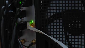 Close-up view of a computer's backside, showing connected cables, glowing indicator lights, and a cooling fan behind a mesh grille. video